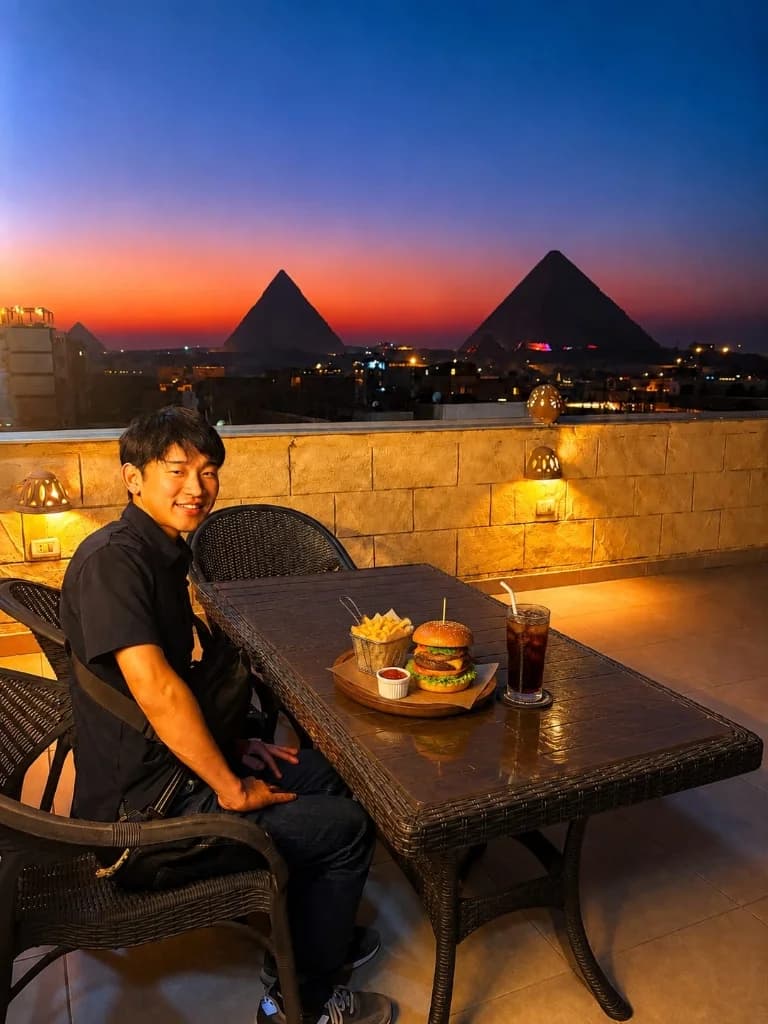 Guest dining at Camel Taste rooftop terrace with sunset view of the Giza Pyramids